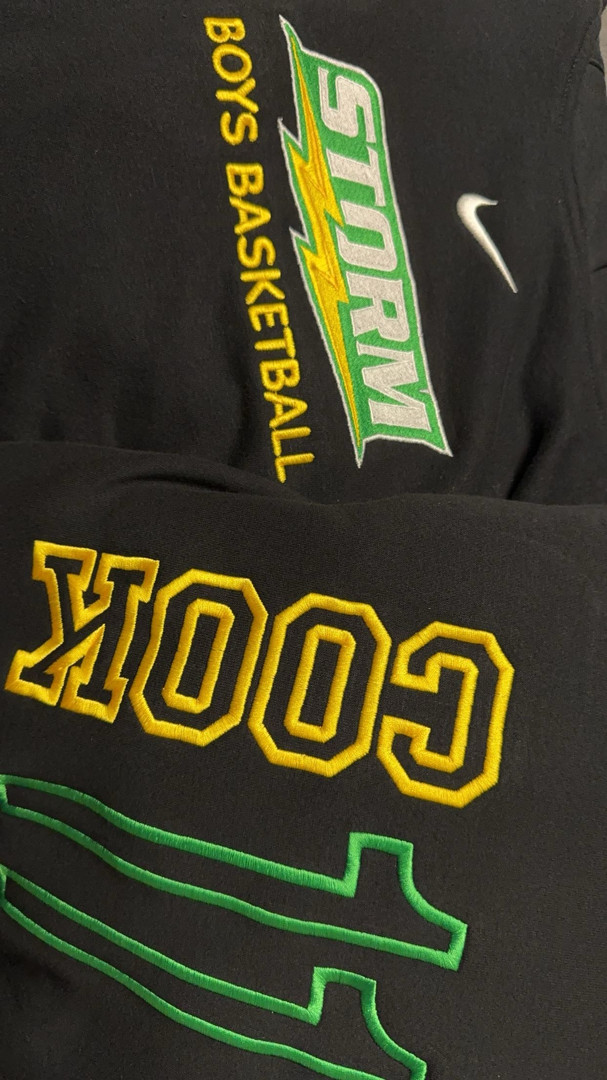 Black apparel with custom embroidery for a boys' basketball team, showcasing vibrant threads and green text and a basketball team logo.